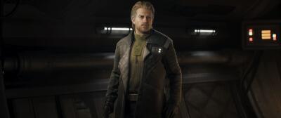 A lone officer in a worn brown coat stands in a dim starship corridor with glowing panels and consoles behind him — Star Wars: Zero Company.