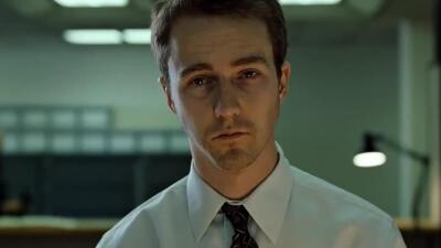 Close-up of a weary man in a white shirt and tie, hollow-eyed under fluorescent office lights — a moody Fight Club scene.
