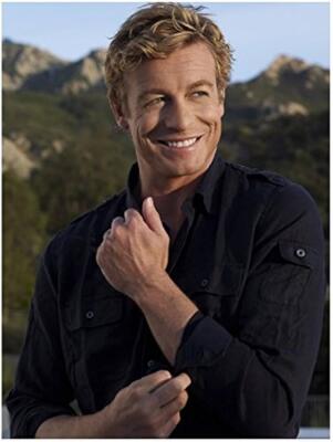 Smiling blond man in a dark button-up shirt outdoors, rolling up his sleeve with sunlit hills in the background.