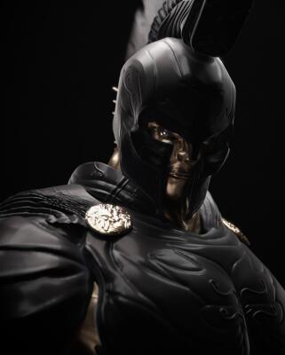 Close-up of a helmeted, black-armored warrior with gold faceplate and ornate shoulder medallions, plume atop helmet, dramatic low-key lighting — The Odyssey (2026)
