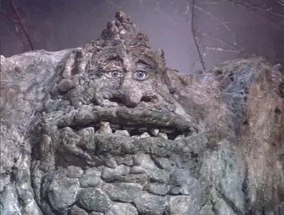 Weathered stone giant face with deep-set eyes, broad nose and jagged teeth — the Rockbiter creature from The NeverEnding Story.