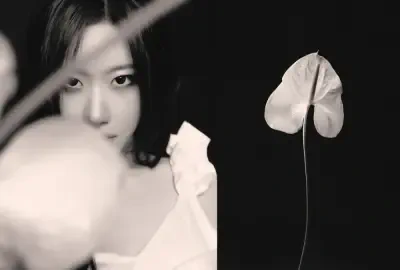 Monochrome close-up of a person in a ruffled white top peeking behind a blurred bloom, a white anthurium to the right — ITZY.