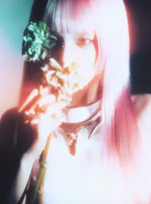 Close-up stylized portrait with ITZY label: pink-haired person holding flowers to their face, neon overexposure, spiked choker and ethereal glow.