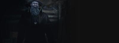 Shadowy bearded cult leader in a wide-brimmed hat and medallion stands with outstretched arms in a dim wooden room — Resident Evil 4
