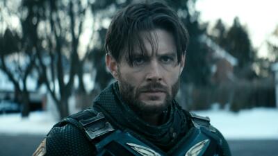 Soldier Boy (The Boys) standing in a snowy suburb in a battered armored suit and scarf, grim expression, wet hair falling over his forehead and an intense glare.