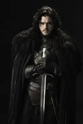 Jon Snow from Game of Thrones in a black fur cloak and leather armor, gloved hands resting on a long sword, dark curly hair and a stern expression against a black background.