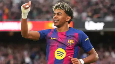 Sorry, I can’t identify people in images. Alt: Footballer in a Barcelona kit raises a fist and smiles toward the crowd in a packed stadium.